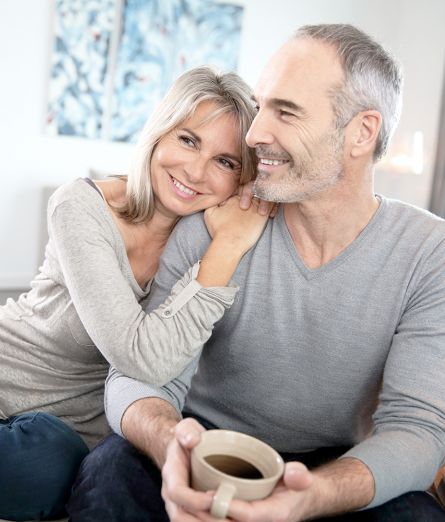 Mann und Frau sitzen mit Kaffee gemütlich und lächelnd auf Couch