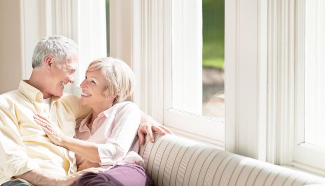Best-Ager-Paar sitzt auf Sofa vor Kunststofffenster