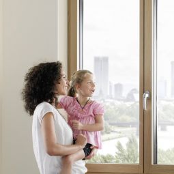 Frau und Mädchen schauen aus UNILUX Holz-Alu-Fenster in die Ferne